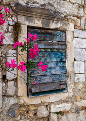 Fototapeta na wymiar Old wooden window with cracked pain,graphite drawings and pink flowers,stone house