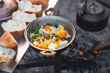 Detail view of camp fire cooking, breads are in a row, a tea pot and onion pan is on the fire with...