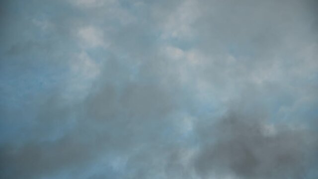 Looking straight up into a teal blue sky filled with translucent white and gray clouds that are moving diagonally.
