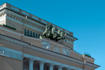 Ostrovsky Square, Saint Petersburg, Russia, 11.10.2020. Ancient green sculpture of cavalry with horses on facade of yellow building of Russian State Drama Theater named Pushkin. Blue sky background