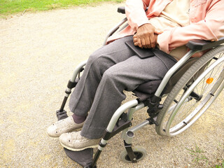 Obraz premium Close-up of the body of an elderly disabled black woman in a wheelchair, holding her phone on her legs