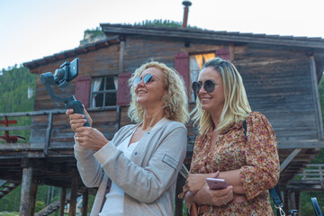Pair of Brazilian blonde women watching phone with house of Lake Braies background, South Tyrol, Italy