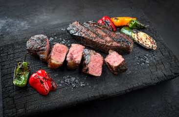 Barbecue dry aged wagyu roast beef steak with paprika and zucchini offered as close-up on a charred wooden board