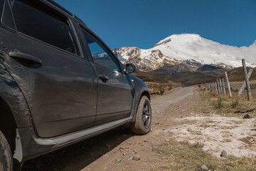 Fototapeta na wymiar a black car, in the field, a dirt road, in the background is a snow-covered mountain, clear sky, sunny day