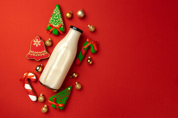 Glass milk bottle and Christmas gingerbread cookies on red background