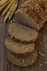 Sliced of cereal bread on wooden table with a bunch of wheat ears,top view