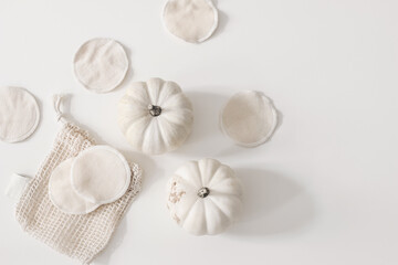 Bio organic cotton reusable round pads for make up removal with pumpkins and knitted bag on white table background. Zero waste concept. Sustainable bathroom and lifestyle. Flat lay, top view.
