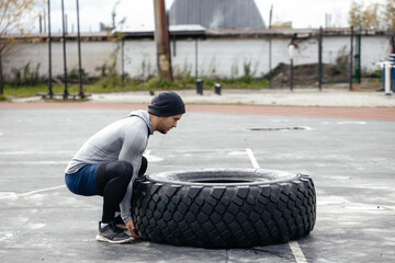 athlete in a headdress is engaged in turning the tire. Sports field, tire turning, full body exercises