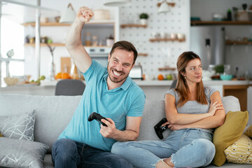 Husband and wife playing video game with joysticks in living room. Loving couple are playing video games at home.