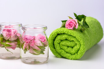 Obraz na płótnie Canvas Green roller towel and pink roses in jars on white isolated background. Spa settings with roses. Fresh rose and .rose heads in jars of water.