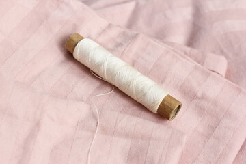 A spool of beige silk thread was forgotten on the bed in the room. A background of pink sheets. You...