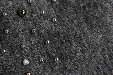Sewn-on metal fittings on gray woolen jersey are present as a background.