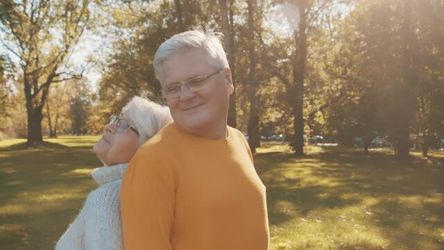 Love and affection at old age. Retired couple enjoying autumn day in forest staying back to back and smiling. High quality 4k footage