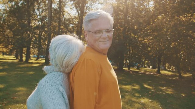 Love and romance at old age. Retired couple enjoying autumn day in forest staying back to back and smiling. High quality 4k footage