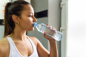 Side view close up on young adult caucasian female drinking water at gym in day - copy space