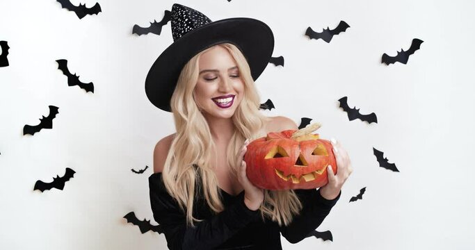 Halloween traditions. Adorable blonde woman in witch costume posing with carved jack-o-lantern pumpkin
