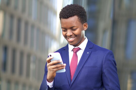 Portrait of happy positive handsome businessman, young black African Afro American man looking at screen oh his cell mobile phone and smiling. Good news. Technology, business, smartphone concept. 