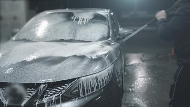 Man washes his car at self-service car wash, covers car with washing foam.