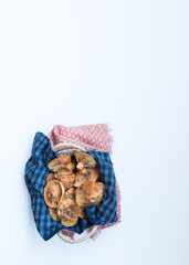 A few saffron milk cups inside a basket covered with a blue and a red fabric napkins. It's placed in the bottom part of the image in the white background.