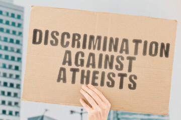 The phrase " Discrimination against atheists " on a banner in men's hand with blurred background. Religion. Belief. Atheism. Disbelief. Decision. Human rights