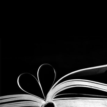 Book pages in the shape of heart on black background with copy space. Creative love background concept.