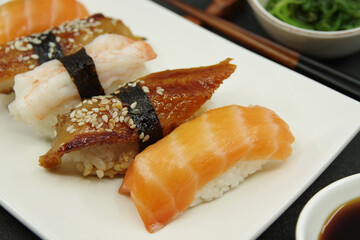 Salmon nigiri, shrimp nigiri, unagi nigiri. Japanese sushi food on a white plate, served with ginger and seaweed salad. 