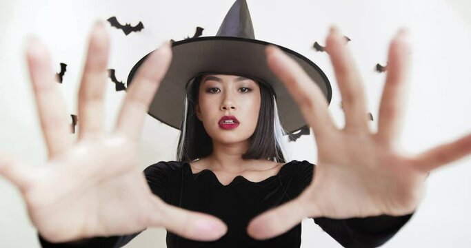 Asian woman in black witch costume casting spell to camera, Halloween magic concept