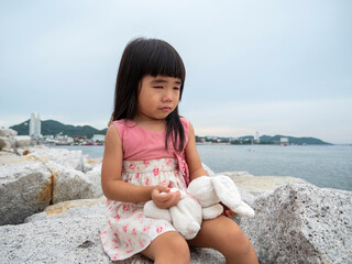 Little girl crying and hug the rabbit doll  by the sea in a sad mood and missed her family