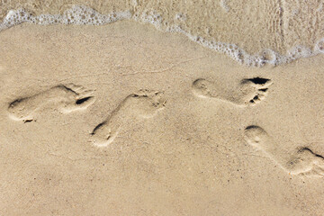 Photo of a sunny day sea shore footsteps printed on sand.