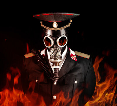 Photo of a post apocalyptic military officer in uniform suit and peaked cap standing in soviet gas mask in fire.