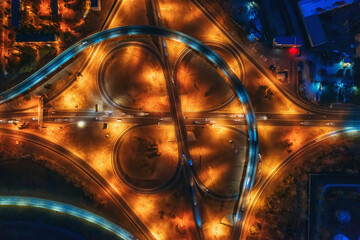Large roundabout or road transport junction at night with car traffic, aerial top view.