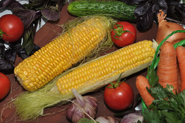 Fototapeta na wymiar Ripe corn and fresh vegetables on a cutting board