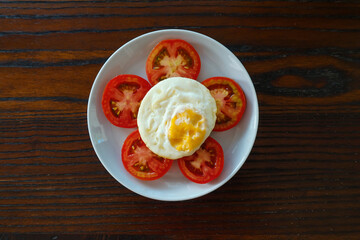 Fried egg served with slice fresh tomato on white plate and wooden table 
