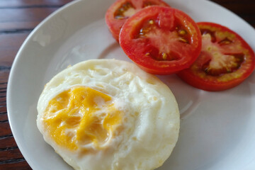 Fried egg served with slice fresh tomato on white plate and wooden table 