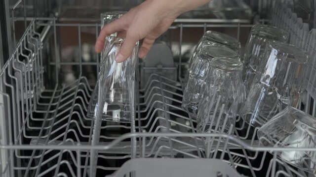 New dishwasher appliances. A woman puts glasses into a dishwash machine in the kitchen. A concept of modern appliences in the kitchen.