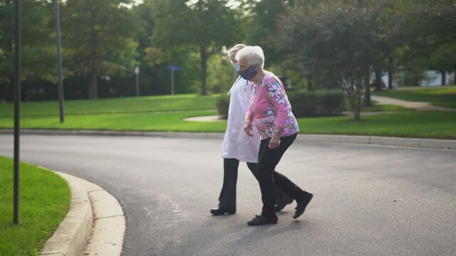 Wearing face masks, woman doctor caregiver help elderly old senior grandmother patient walk outside retirement house, female doctor carer provide elderly lady medical service, older healthcare concept