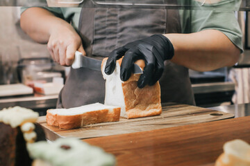Hand wearing glove with a knife cuts loaf of bread on a wooden board.Fresh bread on the kitchen table The healthy eating and traditional bakery concept
