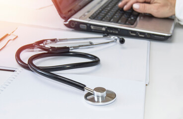 Medical concept, stethoscope lying on the table at the doctor's workplace, in the background the doctor's hand of a woman using a laptop