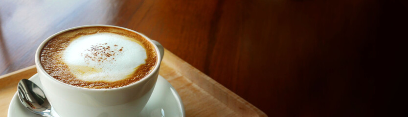 Closeup hot cappuccino coffee cup on dark wooden table with copy space as banner background