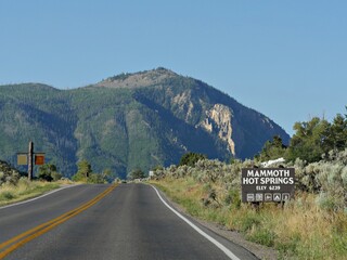 Upward road with a tall mountain the the distance, with a roadside sign to Mammoth Hot Springs at Yellowstone National Park.