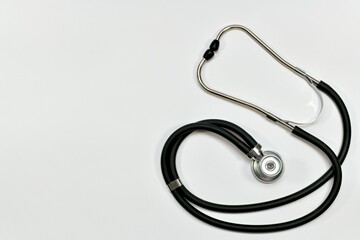 A medical stethoscope with a black hose, a membrane and headphone pads. On the bright background on the whole one.