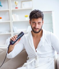 Fototapeta premium The young man drying hair at home with a hair dryer blower