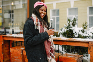 Cute black woman have fun in a city. Beautiful black girl in a pink beret. Stylish lady drinking a coffee