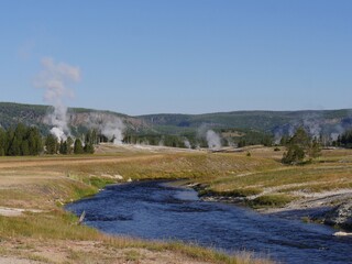 Wide shot of the Firehole River with hot water overflow and steam rising from multiple geysers at the Yellowstone National Park in Wyoming.
