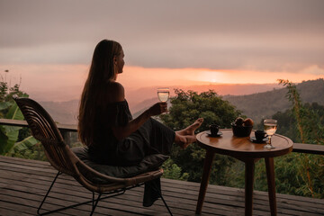Young woman enjoying glass o white  wine on the roof by the mountain terrace  at sunset