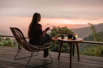 Young woman enjoying glass o white  wine on the roof by the mountain terrace  at sunset