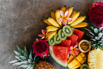 Fototapeta na wymiar Tropical fruits assortment on a wooden plate. Stone background. Top view. Copy space.