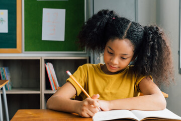 African American school girl sitting in school writing in note book with pencil, studying, education, learning. Female student at desk in classroom in exam. - 384670951