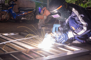 The welder is welding the parts of the iron door. The person working on a welder using an electric welding machine.