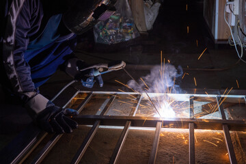 The welder is welding the parts of the iron door. The person working on a welder using an electric welding machine.